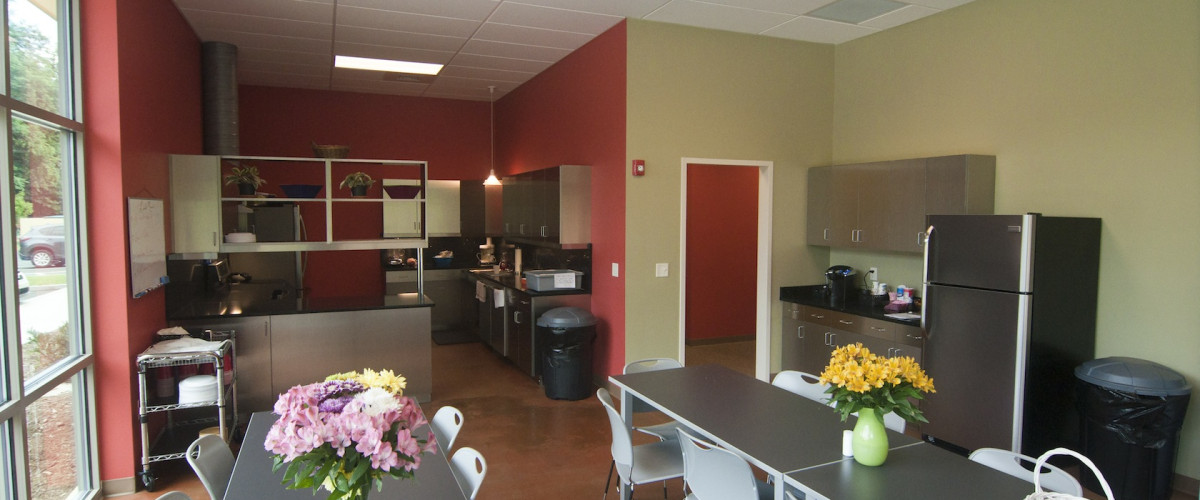 A kitchen with tables and chairs, refrigerator, microwave, and other items.