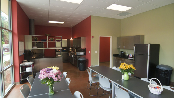 A kitchen with tables and chairs, refrigerator, microwave, and other items.